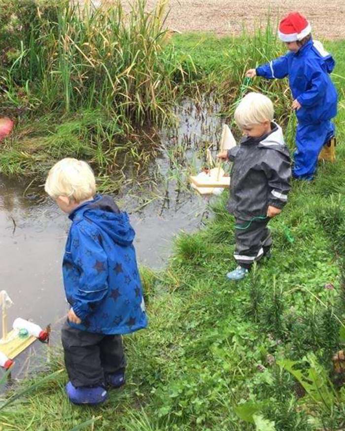 Fire børn med små tømmerflåder ved vandløb